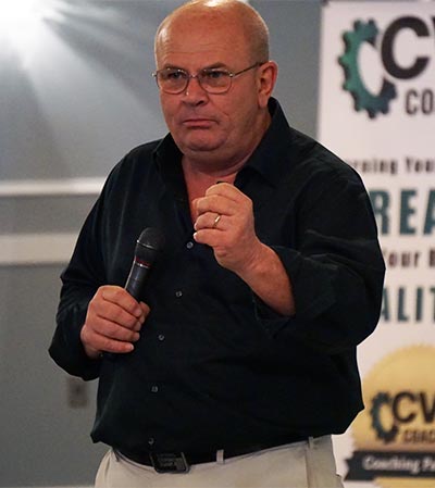 Jerry Isenhour speaking with microphone in his hand wearing glasses with CVC banner in the background