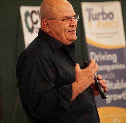 Jerry Isenhour speaking at a conference he has glasses and a microphone in his hand.