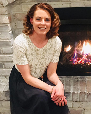 Brandi Biswell, Chimney & Fireplace Success Network host sitting on fireplace hearth shoulder length auburn hair
